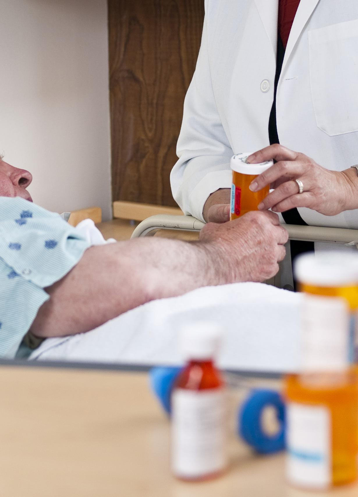 a pharmacist holds a medication bottle at a patient's bedside.