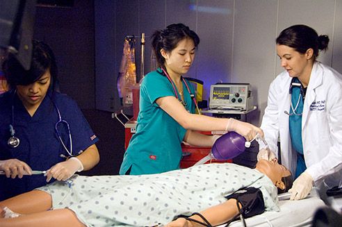 team members perform a simulation around an artificial patient lying on a bed