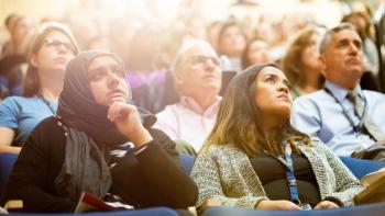 Two women watching a presentation while sitting in a crowd
