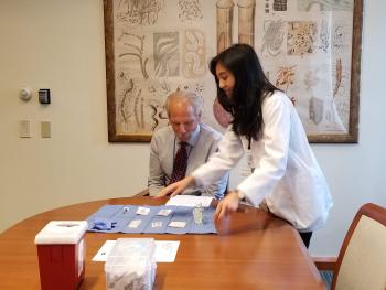 Agustin, standing, with Guglielmo, seated at table with vaccine materials